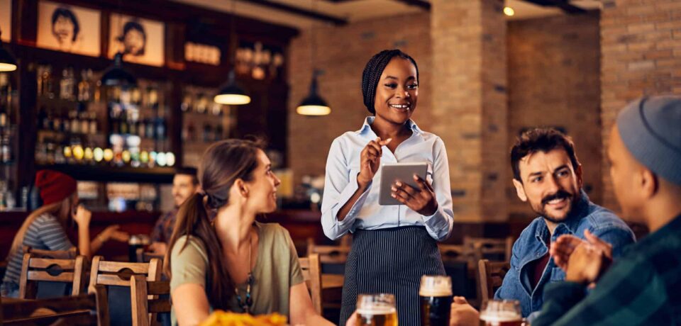 Eine Servicekraft nimmt in einem gemütlichen Restaurant mit Tablet Bestellungen von Gästen auf. Das Bild steht für moderne Gastronomie, digitale Bestellaufnahme, professionellen Service, Restaurantbetrieb, Reservierungen und digitale Abläufe in Restaurants.