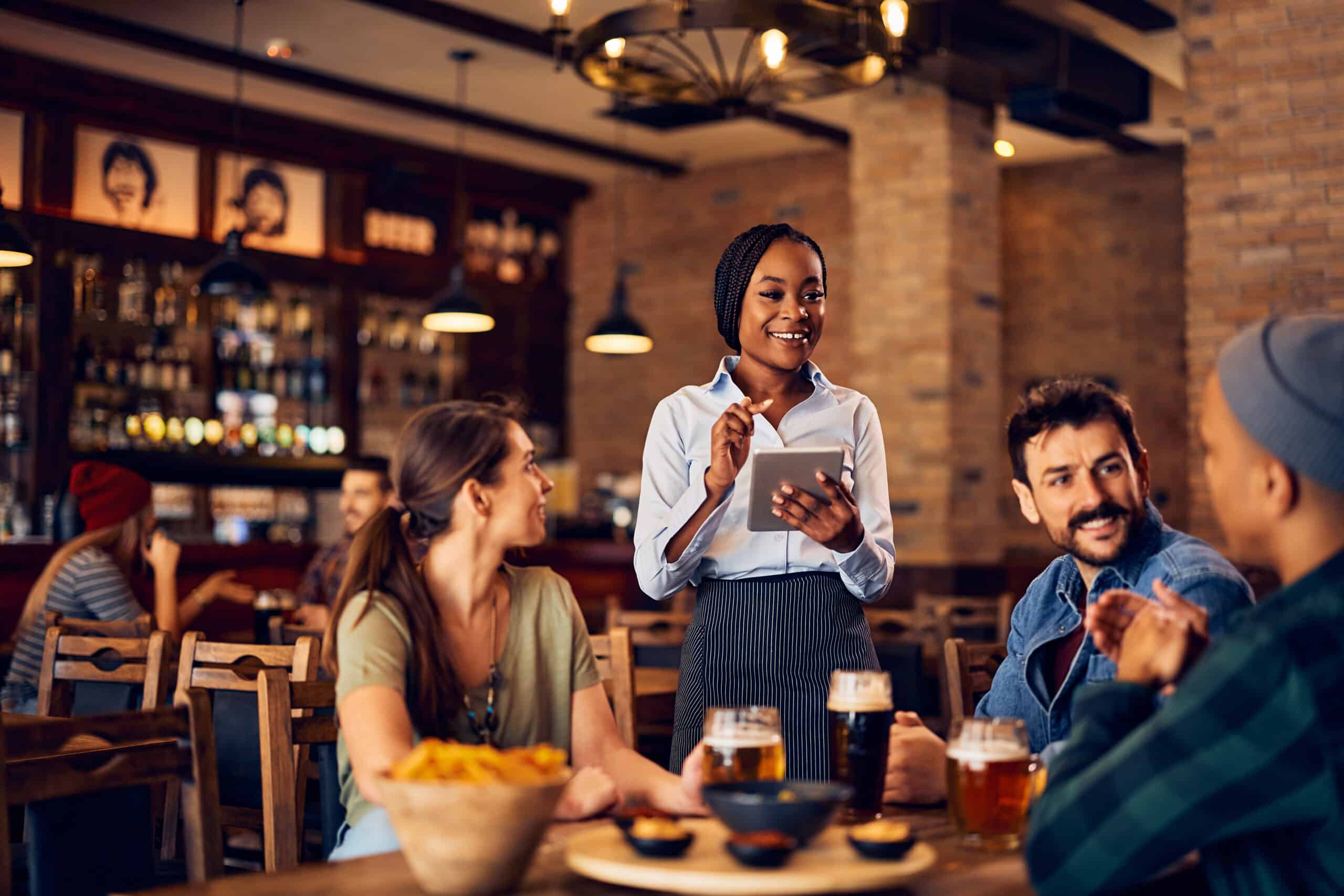 Eine Servicekraft nimmt in einem gemütlichen Restaurant mit Tablet Bestellungen von Gästen auf. Das Bild steht für moderne Gastronomie, digitale Bestellaufnahme, professionellen Service, Restaurantbetrieb, Reservierungen und digitale Abläufe in Restaurants.