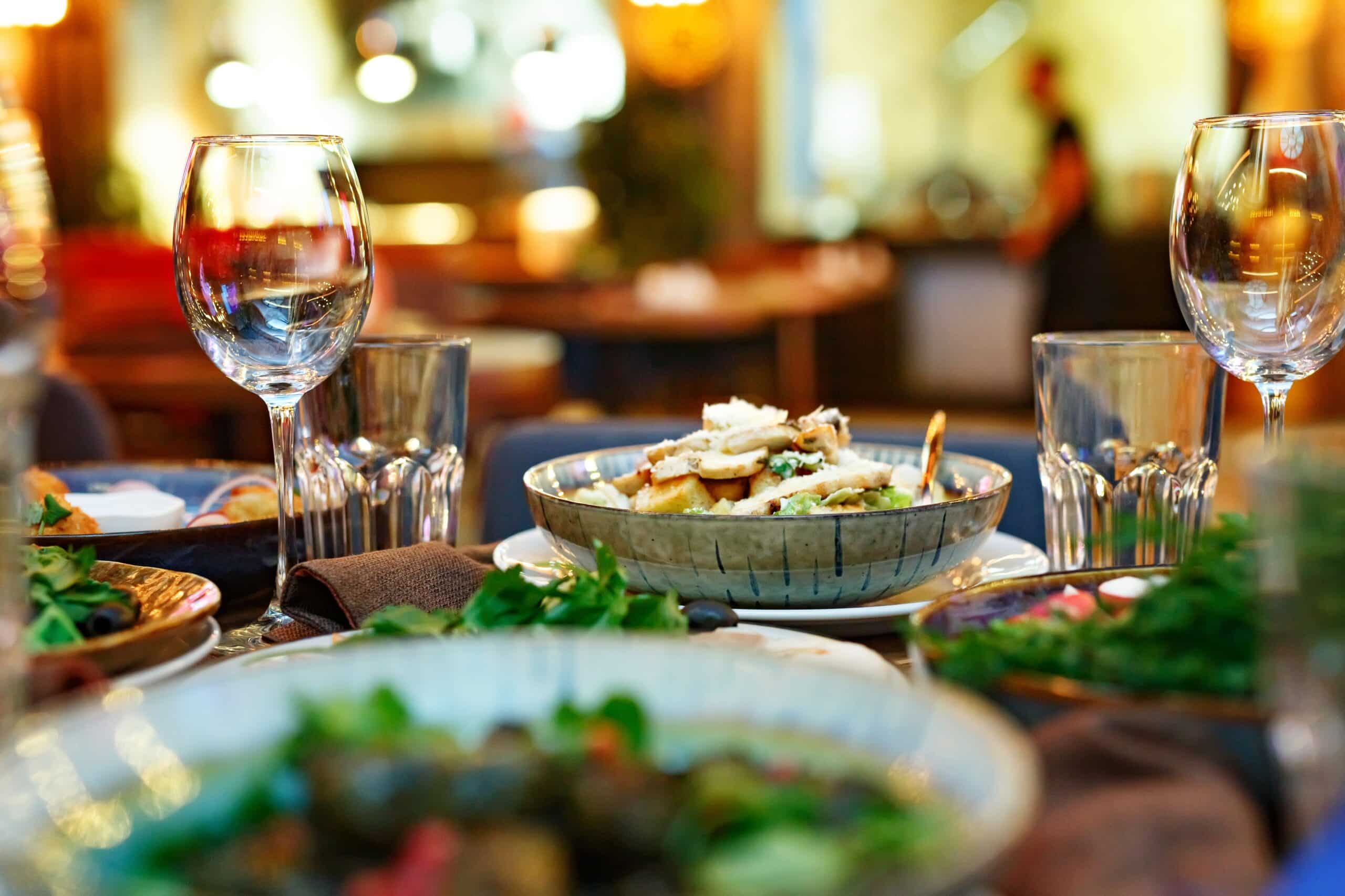 Ein stilvoll gedeckter Tisch mit Gläsern, Speisen und warmer Restaurantbeleuchtung schafft eine einladende Atmosphäre.